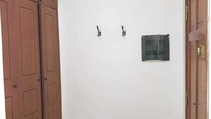 A room with a large wooden door on the left, a smaller door on the right, and a white wall with two wall hooks and a small plaque.