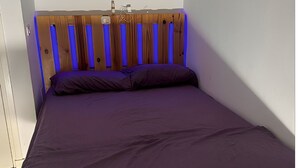 A bedroom with a wooden headboard, a purple bedspread, and a white wall.