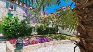 A courtyard with stone walls, flowering plants, and a palm tree. - Nirvana Garden Rooms (Split)