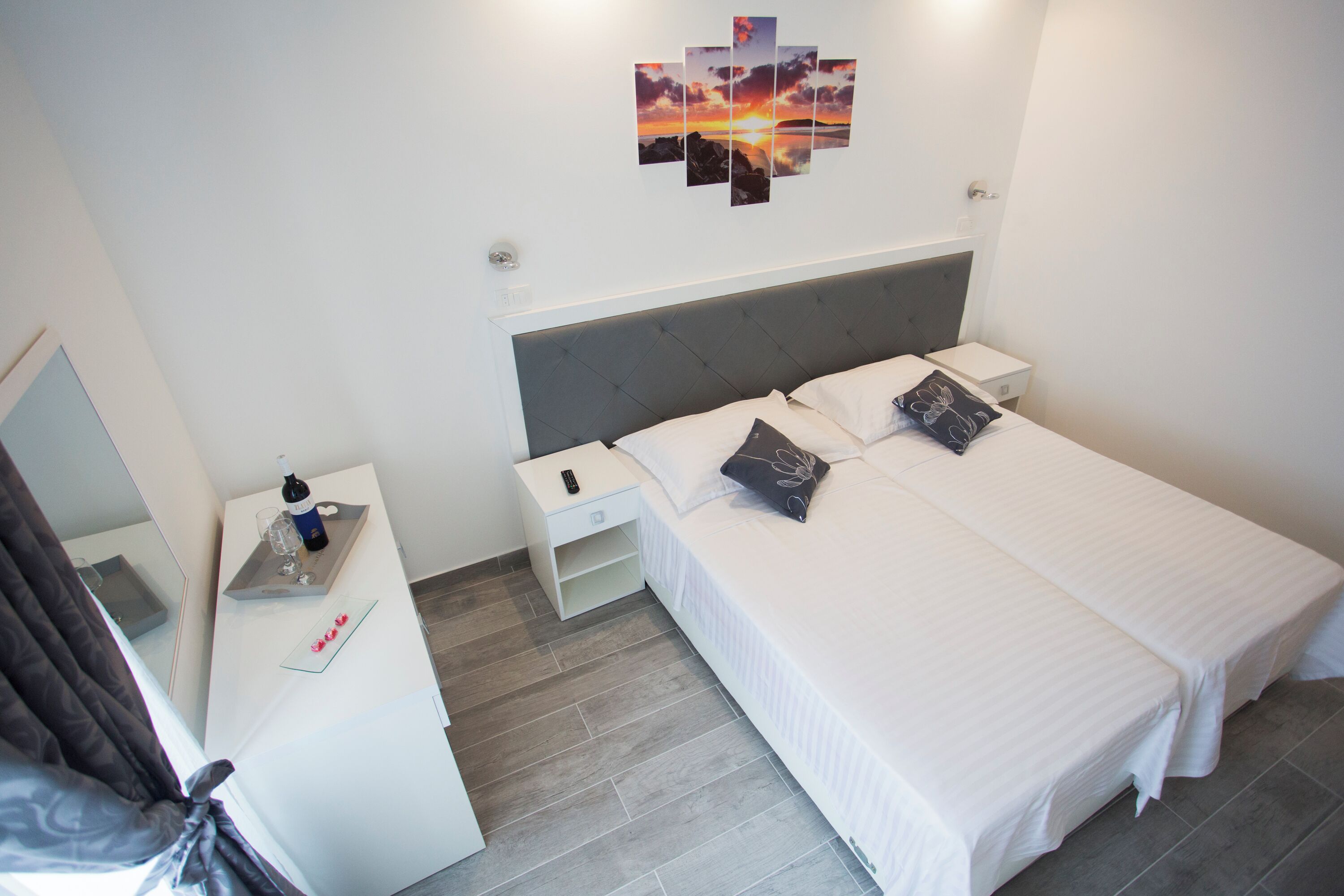 A hotel room with a bed, bedside tables, a nightstand, a wall-mounted artwork, and a mirror.