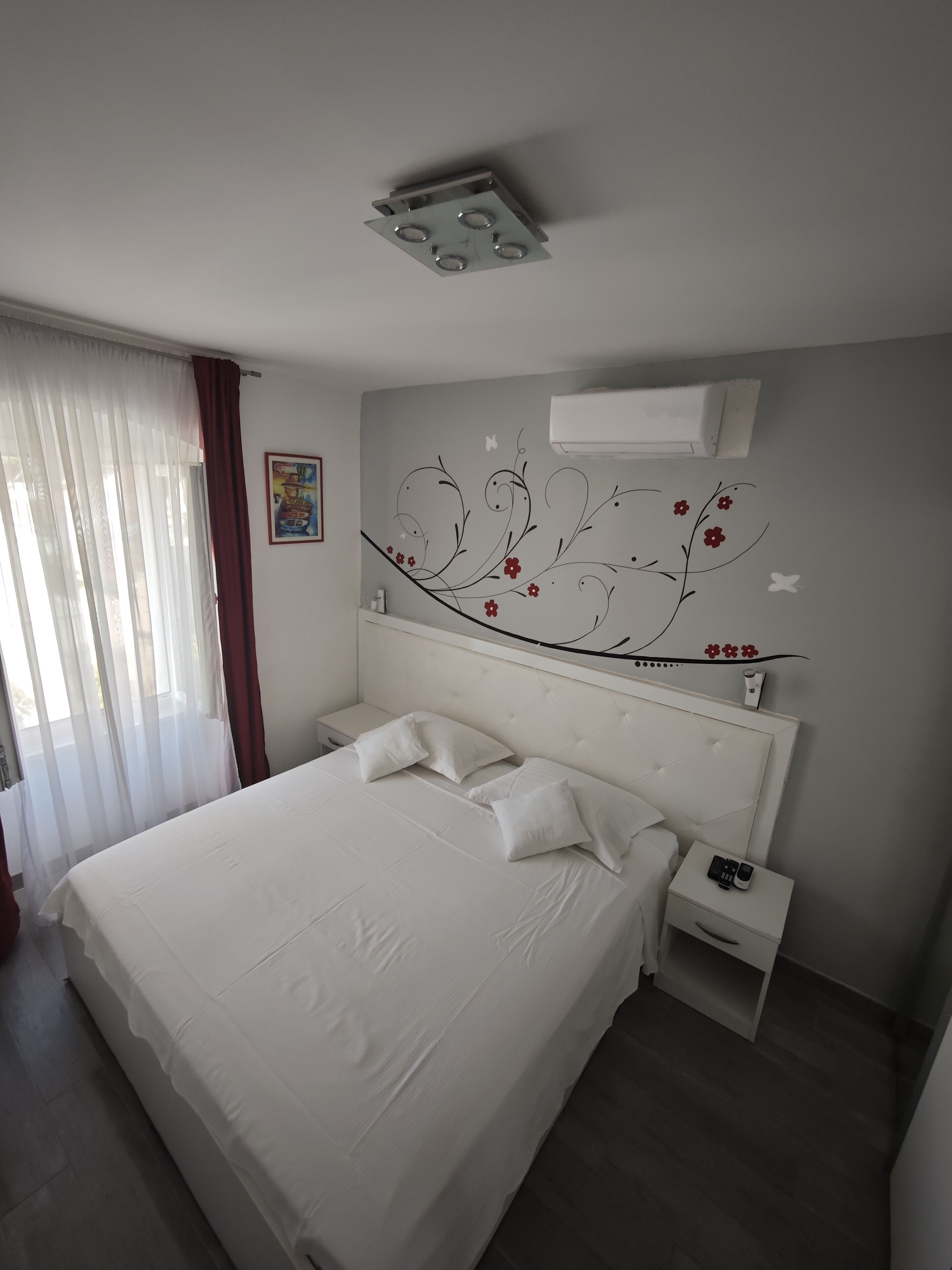 Un dormitorio con cama blanca, cabecero con diseño floral, mesita de noche y velador.