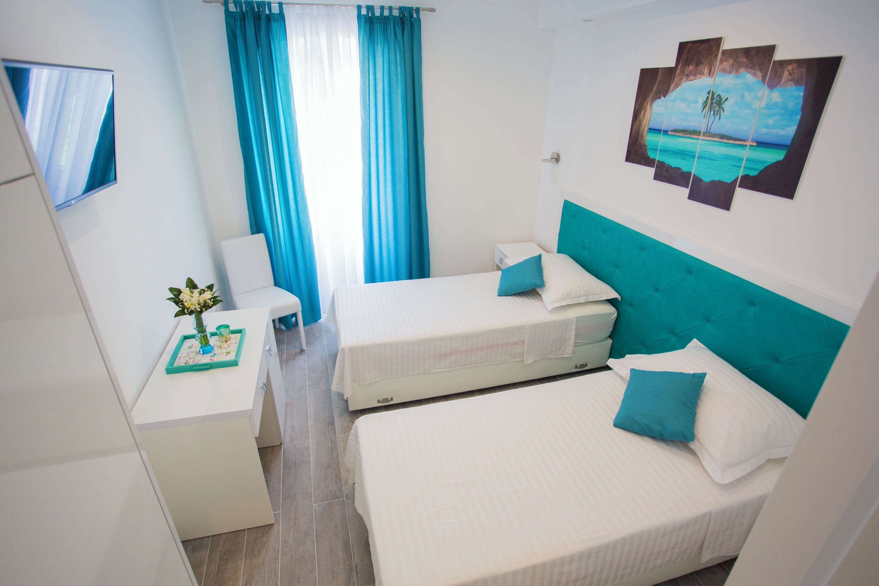 Une chambre avec deux lits, un bureau, une chaise, un téléviseur et un tableau représentant une scène de plage.
