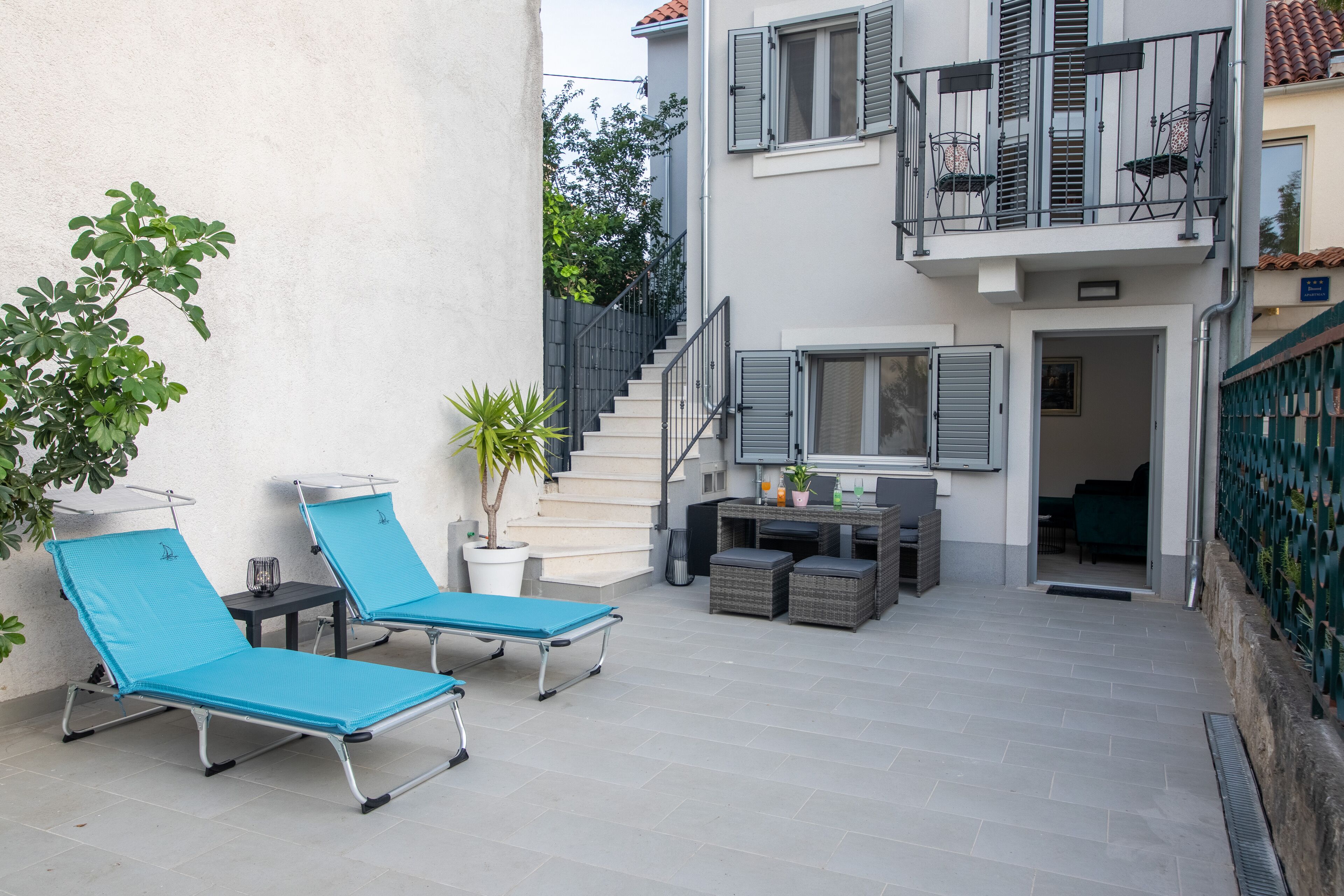 A courtyard with two blue lounge chairs, a small table, and a potted plant.