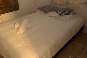 A neatly made bed with a white duvet, two rolled white towels, and two checkered pillows.