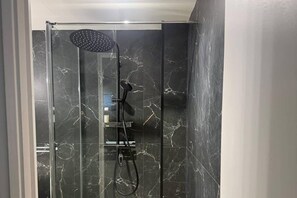 Divisória de chuveiro moderna com chuveiro manual e painel de controle fixado na parede.