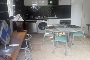 Eine kleine Küche mit Waschmaschine, einem Esstisch mit Stühlen und einer Lampe.