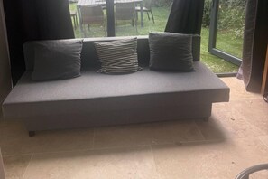A grey sofa with cushions, positioned in a room with a view of a grassy area outside.