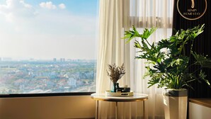A room with a large window, a small round table with a vase and a plant, and a logo on the wall.