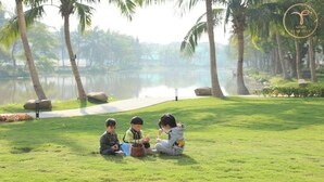 A group of children sitting on grass near a lake with palm trees in the background.