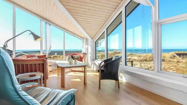 Una habitación amplia con ventanas grandes, techo de madera y vista a la playa.