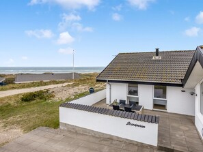 Una casa costera con techo de tejas, un patio con mobiliario exterior y vista al mar.