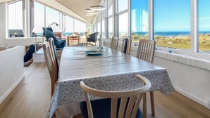 Un comedor con una mesa larga, sillas y ventanas amplias que dan a la playa.