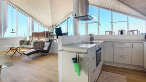 Una cocina moderna con una isla grande, armarios blancos y vistas amplias a través de ventanales.