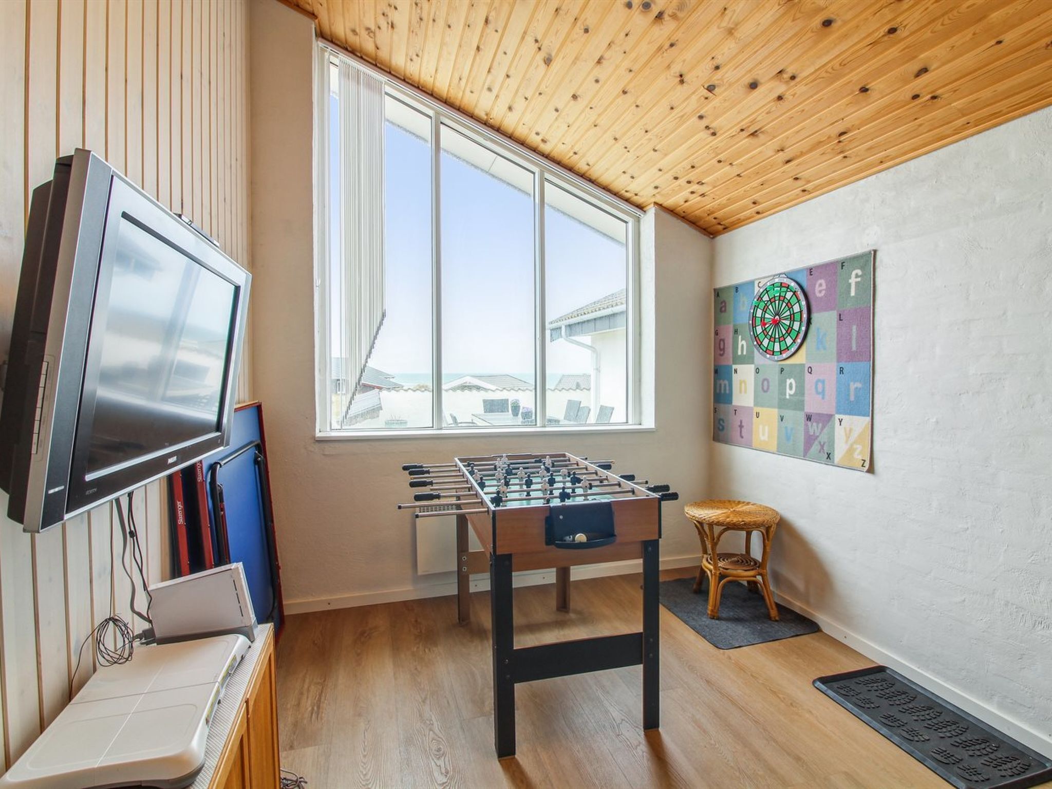 Een kamer met een tafelvoetbaltafel, een televisie en een raam met uitzicht op gebouwen.