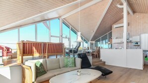Un interior moderno con techo de madera, ventanas amplias, sofá, comedor y cocina.