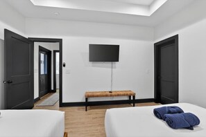 A hotel room with two beds, a bench, a TV, and a door leading to a hallway. - Heart of Downtown Chattanooga | Sleeps 8 | Pool Table (Chattanooga)