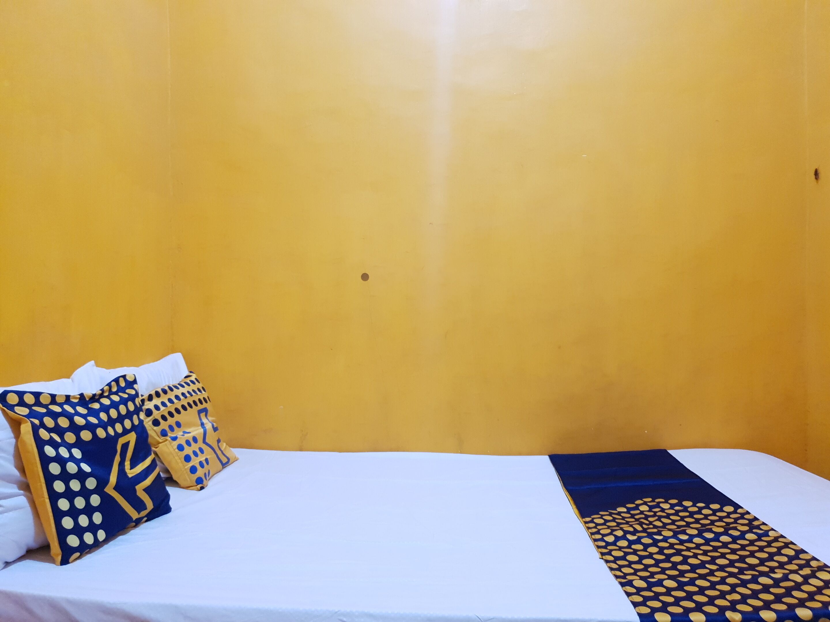 A bed with white bedding, two pillows with yellow and blue patterns, and a blue and yellow blanket.