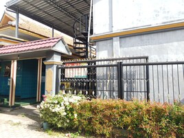 Un edificio con una escalera de metal, una entrada con portón y una pequeña tienda con techo rojo.