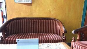 Une pièce avec un canapé en bois et un fauteuil assorti, une petite table avec un ordinateur portable, et une nappe à motifs floraux.