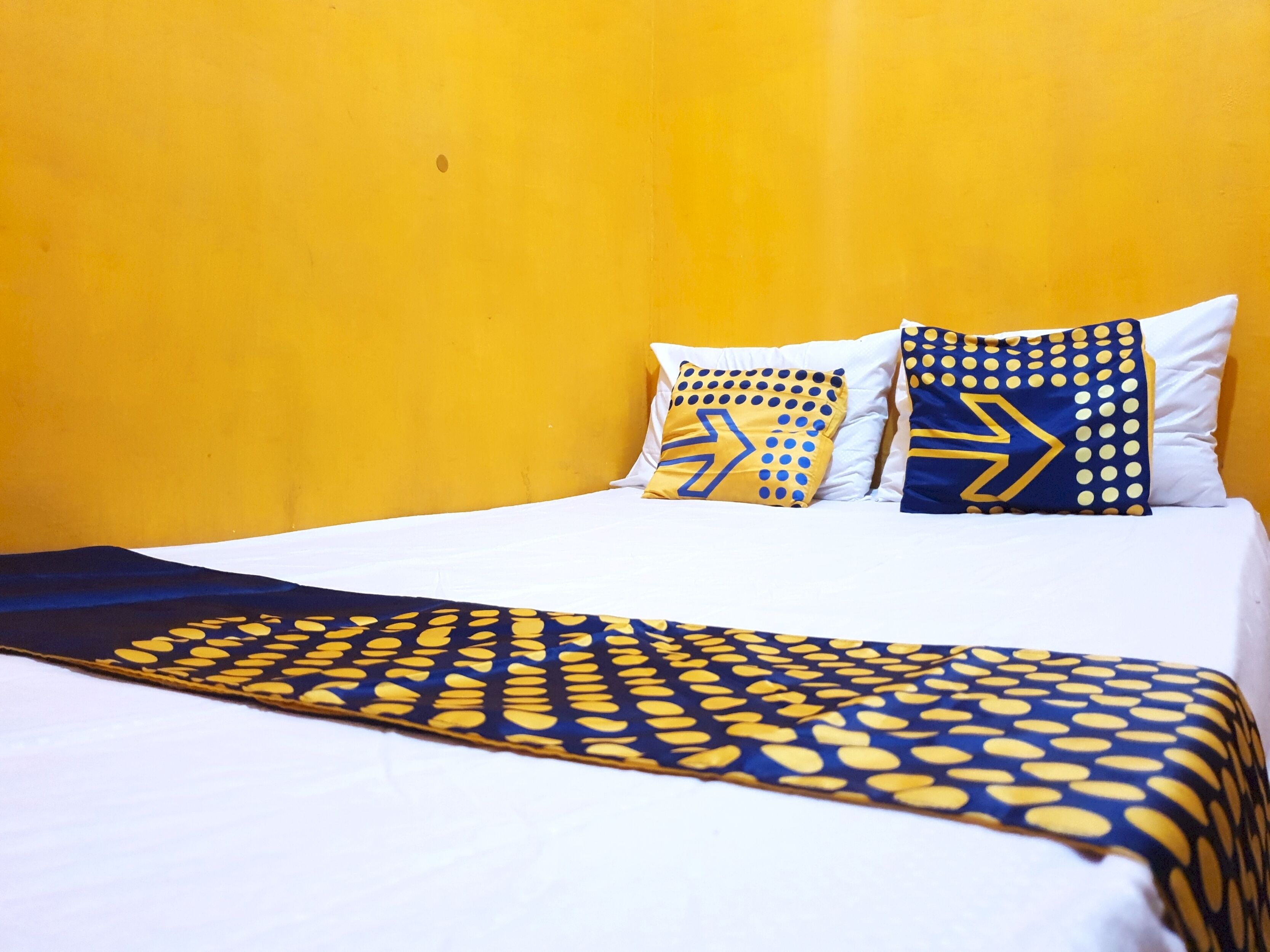 Un lit avec une literie blanche et deux coussins décoratifs aux motifs géométriques.