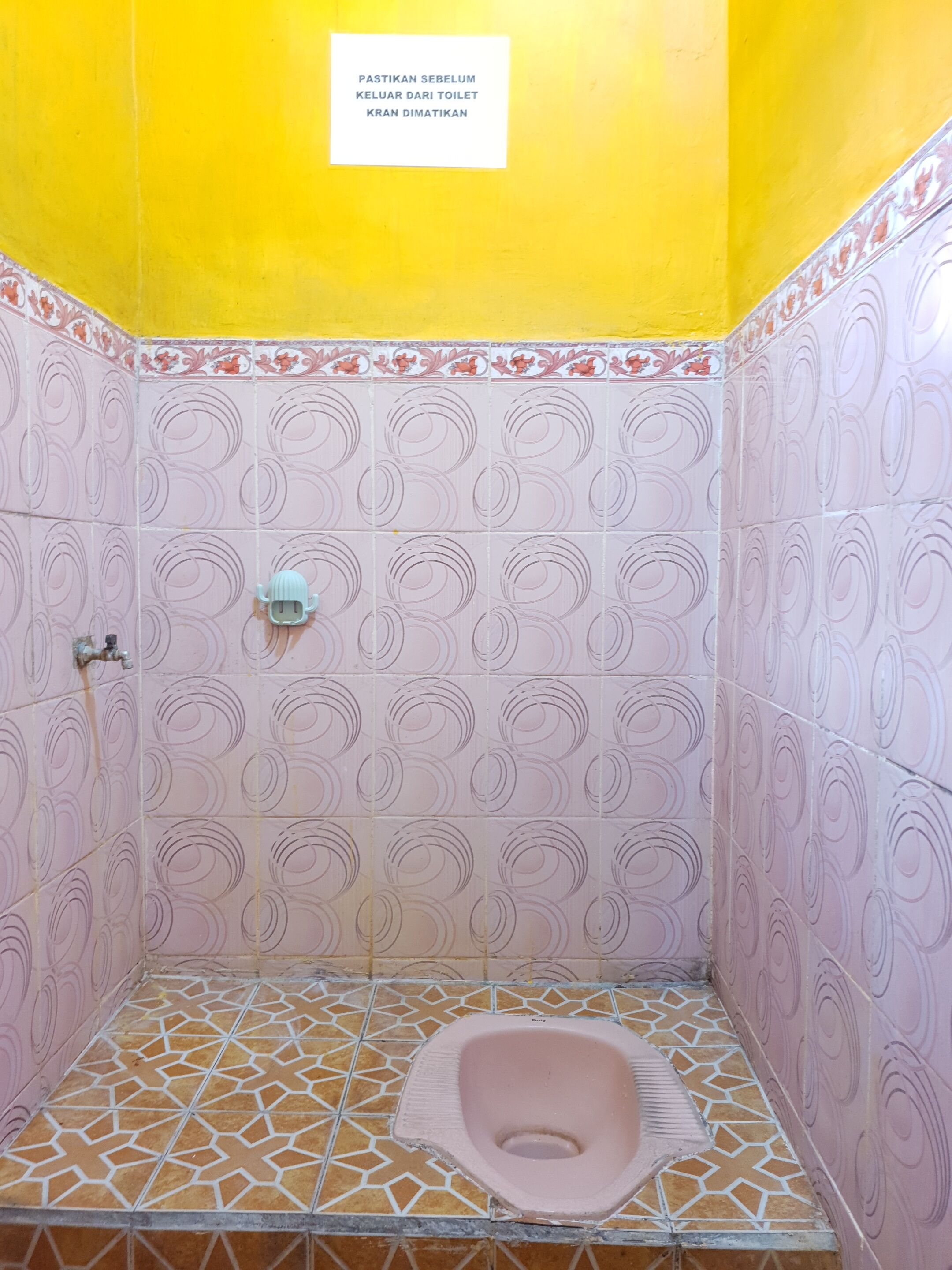 A small, tiled bathroom with a toilet, a hand dryer, and a sign in a foreign language.