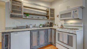 A kitchen with a dishwasher, stove, microwave, and open shelves with dishes.