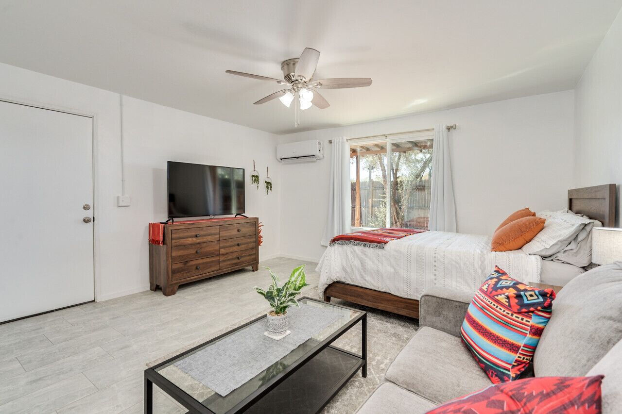 A modern bedroom with a bed, a TV, a ceiling fan, and a window with curtains.