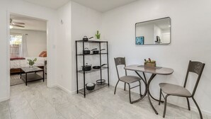 A compact living space with a kitchenette, a dining area with two chairs, a small table, and a metal shelf unit with pots and pans.