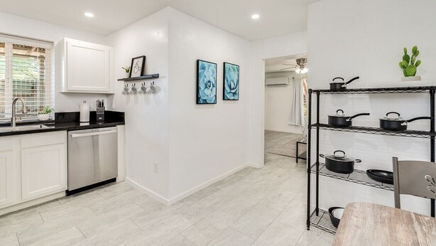 A modern kitchen with white cabinetry, a black countertop, and a pot rack.