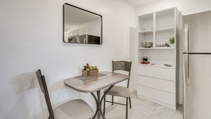 A compact kitchen with a dining table, chairs, a mirror, and a built-in white shelving unit.