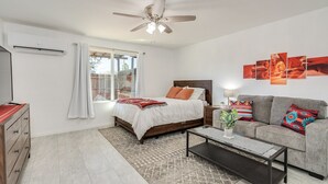 A bedroom with a bed, a grey sofa, a coffee table, and a ceiling fan.