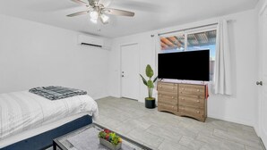 A bedroom with a bed, a ceiling fan, a TV, a dresser, and a window with curtains.