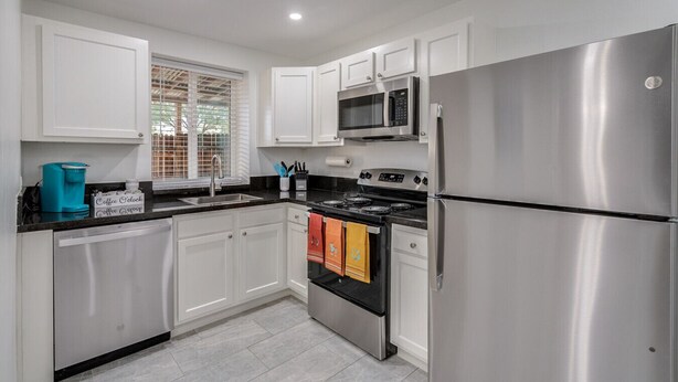 A modern kitchen with white cabinets, stainless steel appliances, and a black countertop.