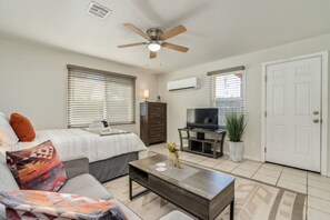 A bedroom with a bed, a desk, a television, and a ceiling fan.
