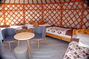 A yurt interior with a bed, two chairs, a small table, and a stool.