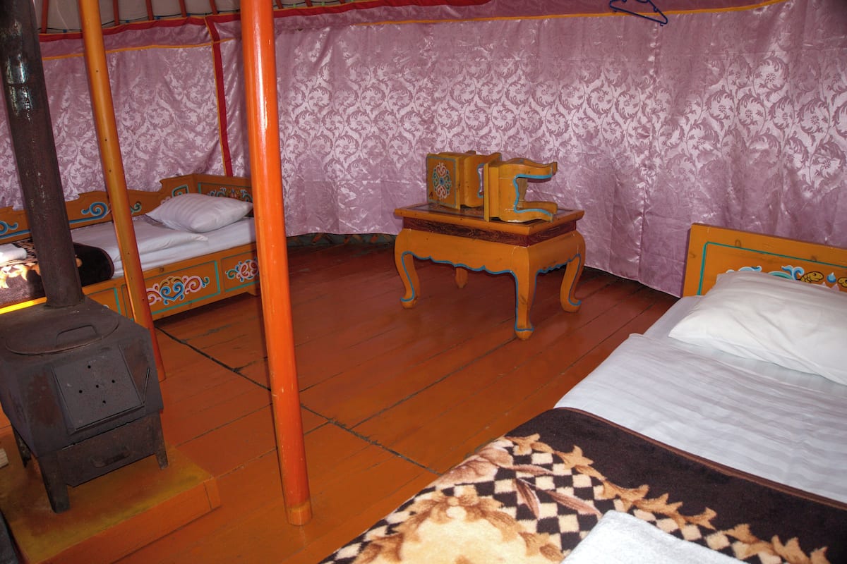 A traditional room with a bed, a small wooden table, and a wood-burning stove.