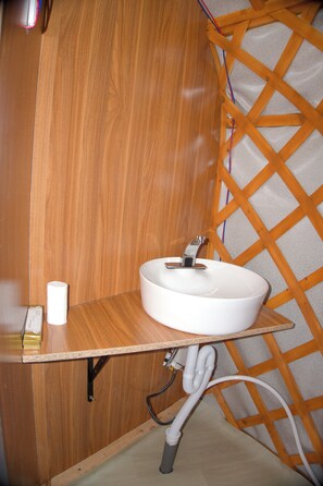 A bathroom with a wooden vanity, a white sink, and a towel dispenser.
