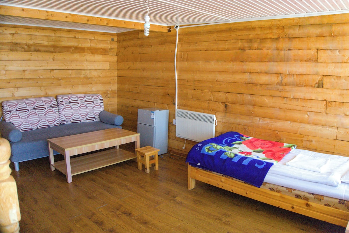 A wooden cabin room with a sofa, a small table, a bed, and a heater.
