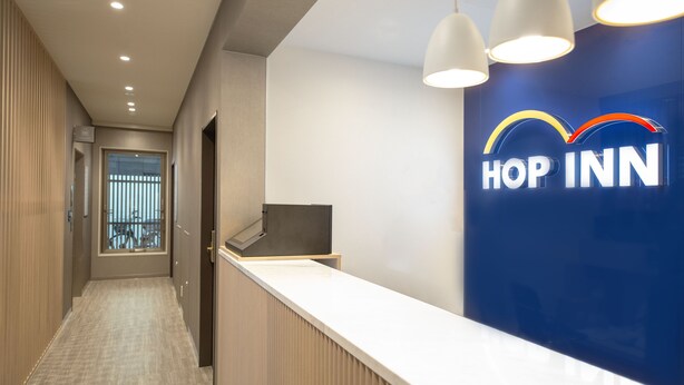 A reception area with a counter, a sign reading "HOP INN," and a view of a balcony through a door. -  HOP INN Tokyo Iidabashi (Tokyo)