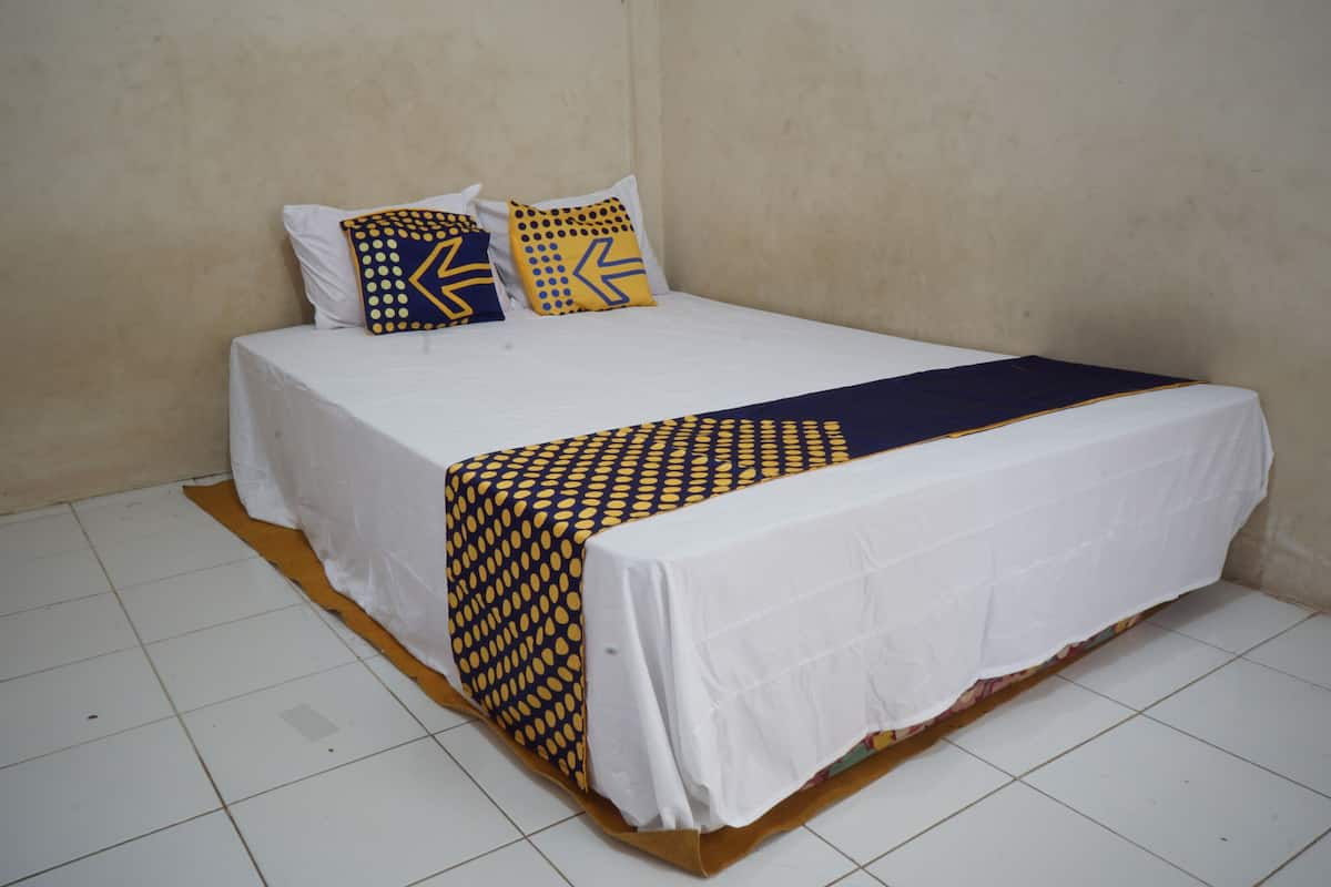 A single-bed room with a white bedspread, two pillows with geometric patterns, and a dark blue throw blanket.