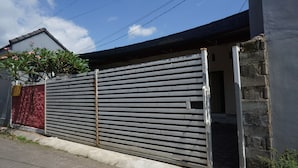 A gated entrance with a metal fence, a concrete pathway, and a building with a grey roof and a red wall. - Hotel O Hunian 99 (Genteng)