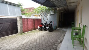 A covered outdoor area with a tiled floor, two motorcycles parked, a green chair, and a small tree. - Hotel O Hunian 99 (Genteng)