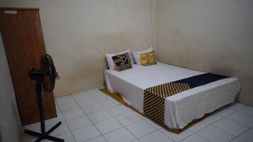 A small, clean room with a bed, a fan, and a wooden door.