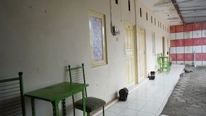 A corridor with green chairs and a table, doors, and a tiled floor. - Hotel O Hunian 99 (Genteng)