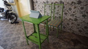 A green metal table with a laptop, a chair with a checkered cushion, and a motorcycle in the background. - Hotel O Hunian 99 (Genteng)