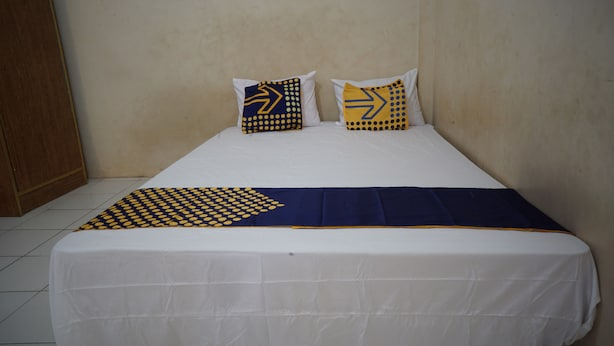 A bed with a white sheet, two pillows with yellow and blue patterns, and a blue blanket with yellow accents. - Hotel O Hunian 99 (Genteng)