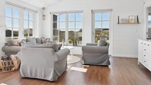 A spacious living room with a grey sofa set, a round coffee table, and a wicker basket. Large windows provide ample natural light and views of the outdoors. - "Ovine" - 300m from the sea by Interhome (Juelsminde)