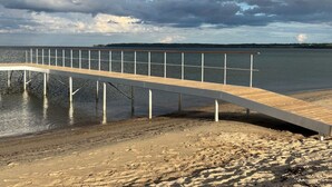 A wooden pier extending over a sandy beach with a calm body of water and a cloudy sky in the background. - "Ovine" - 300m from the sea by Interhome (Juelsminde)