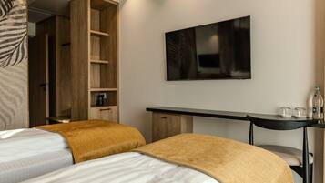A modern hotel room with two beds, a wooden wardrobe, a desk, and a flat-screen TV on the wall.
