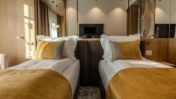 A modern hotel room with two beds, a large mirror, and a television.